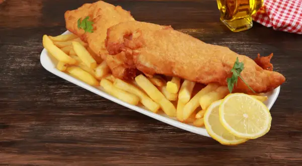 Un delicioso plato típico inglés: pescado rebozado y patatas fritas crujientes, servido con rodajas de limón y perejil.