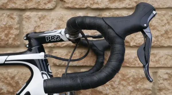 Czarna owijka na kierownicę roweru szosowego z subtelnym wzorem. Widoczna manetka Shimano i mostek PRO.