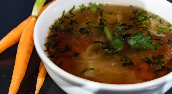 Aromaticzny rosół kolagenowy z marchewką i natką pietruszki, obok świeże marchewki.
