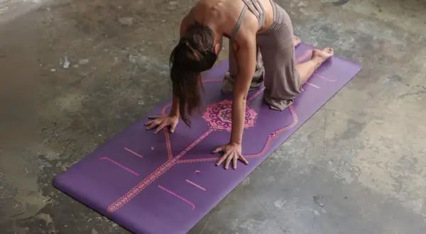 Mujer en postura de la esfinge sobre una esterilla de yoga morada con diseño.