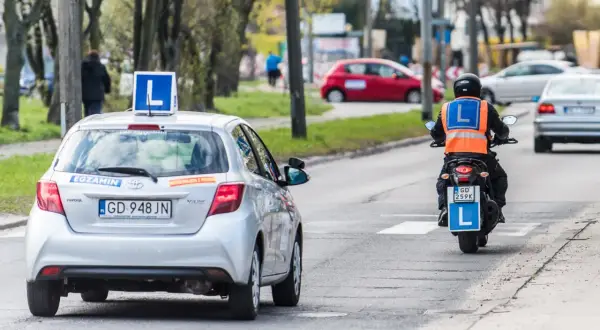 Nauka jazdy na motorowerze, czyli ile kosztuje prawo jazdy AM. Na drodze auto z literą "L" i motocyklista z kamizelką odblaskową.