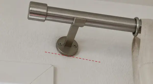 Eine silberne Gardinenstange wird an der Wand befestigt. Die Halterung ist mit Schrauben gesichert.