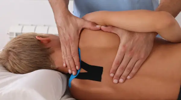 Fizjoterapeuta aplikuje taśmy kinezjotaping na plecy pacjenta.