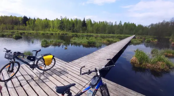 Dwa rowery na drewnianym pomoście nad wodą, otoczone zielenią. Idealne miejsce na odkrywanie tras rowerowych Białystok.