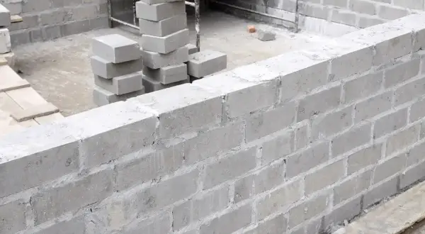 Ściana z bloczków fundamentowych w trakcie budowy. Widać stosy bloczków, gotowe fragmenty muru i zbrojenie. Bloczek fundamentowy wymiary są kluczowe dla stabilności.