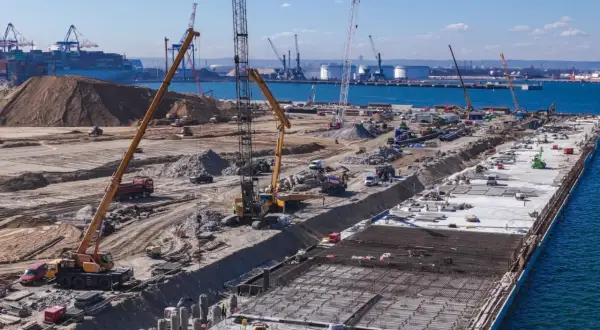 Budowa dużego portu w Japonii. Dźwigi, koparki i ciężarówki pracują na placu budowy, tworząc nową infrastrukturę.