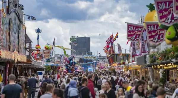Buntes Volksfest mit vielen Menschen, Fahrgeschäften und Buden. Ein Hamburger-Stand ist nicht zu sehen, aber die Stimmung ist ausgelassen.
