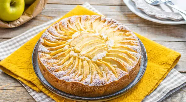 Torta di mele senza zucchero, decorata con fettine di mela disposte a raggiera e spolverata di zucchero a velo.