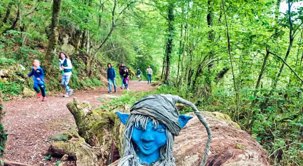 Un duende azul vigila las rutas con niños en Asturias. Familias disfrutan del sendero boscoso.