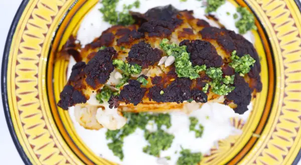 Un chou-fleur rôti, bien caramélisé, servi sur une sauce blanche crémeuse et garni d'une sauce verte et de graines.