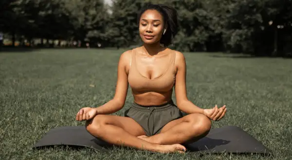 Femme méditant en plein air, une posture de yoga pour maigrir. Elle est assise sur un tapis dans l'herbe, les yeux fermés, en pleine concentration.