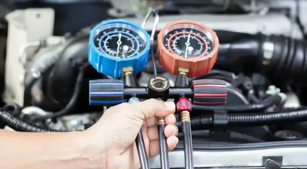 Ręka mechanika trzyma manometr do serwisu klimatyzacji samochodowej. Sprawdź nasz cennik usług.