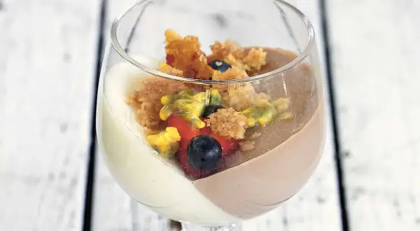 En vacker pannacotta tårta i glas med bär och smulor.