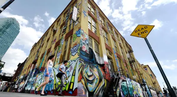 Gelbes Gebäude mit Graffiti-Kunst, Menschen gehen vorbei, "DEAD END"-Schild.