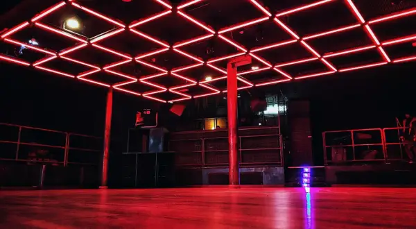 Interno di un basic club con luci al neon rosse sul soffitto e pavimento in legno.