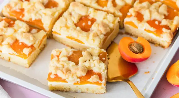 Saftiger aprikosenkuchen mit buttrigen streuseln, perfekt für den Sommer. Ein Stück ist mit einem goldenen Kuchenheber herausgenommen.