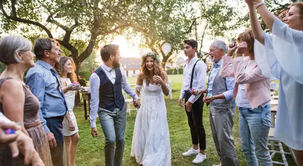 Ein glückliches Brautpaar, schick legere gekleidet, wird von seiner Familie im Garten gefeiert.
