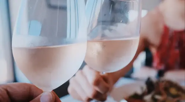 Dwie osoby wznoszą toast kieliszkami z różowym winem. Idealny sposób, jak podawać wino na romantyczną kolację.
