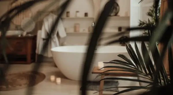 Une baignoire îlot blanche dans une **chaleureux salle de bain zen**. Un peignoir blanc est suspendu, des bougies allumées et des plantes apportent une touche de sérénité.