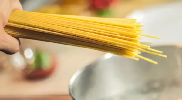 Dłoń trzymająca pęczek spaghetti nad gotującą się wodą. Zastanawiasz się, jaki makaron ma najmniej kalorii?