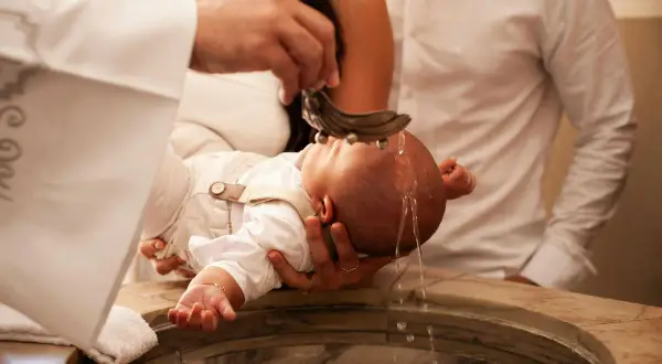 Cérémonie de baptême : un bébé reçoit de l'eau bénite. Le prêtre qui lit le psaume baptême bénit l'enfant.