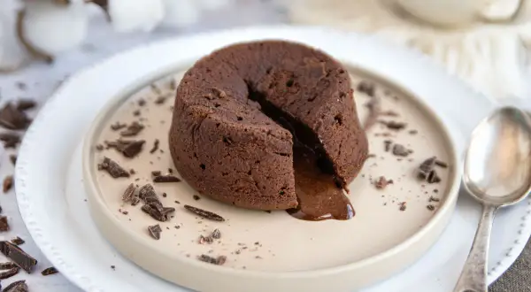 Ein warmes Schoko Soufflé mit flüssigem Kern, garniert mit Schokostückchen auf einem Teller.