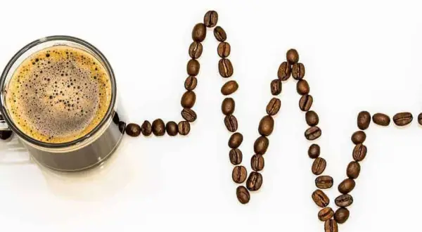 Tazza di caffè con chicchi disposti a formare un elettrocardiogramma, simbolo della caffeina nel caffè che stimola il cuore.