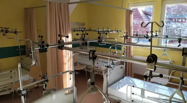 Szpitalna sala z łóżkami i aparaturą ortopedyczną.