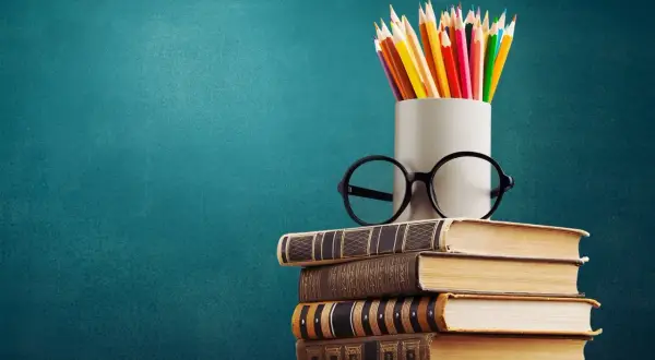 Stos książek, okulary i kolorowe kredki symbolizują drogę do wiedzy, która zaczyna się od wykształcenia średniego.