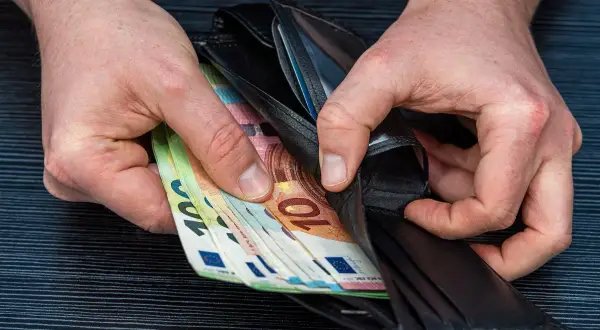 Ręce wkładają do portfela banknoty euro. Zarobione pieniądze po ciężkiej pracy lakiernika.