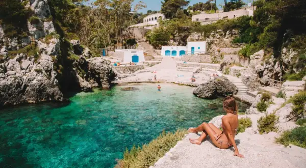 Una donna ammira le zone più belle della Puglia: una caletta con acqua cristallina, rocce e piccole case bianche.