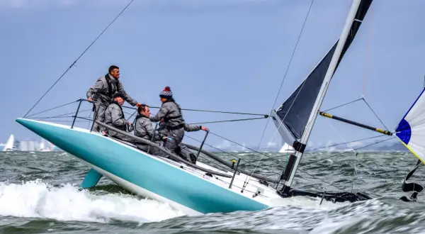 Equipaggio su barca a vela con spinnaker in azione, solcando onde agitate.