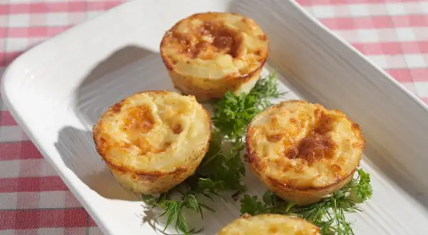 Små, gyllene potatis i muffinsform, serverade med färska örter på en vit bricka. Perfekt som tillbehör eller plockmat.