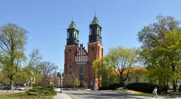 Imponująca katedra w Poznaniu z dwiema wieżami i zielonymi dachami, otoczona drzewami i budynkami.