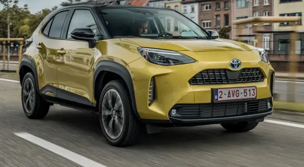 Żółty Toyota Yaris Cross używane na drodze, z czarnym dachem i felgami. W tle widać zabudowania miejskie.