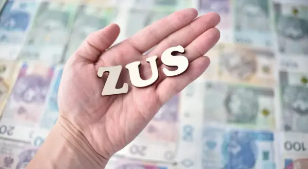 Dłoń trzyma litery ZUS na tle polskich banknotów. Planujesz składki ZUS 2026?