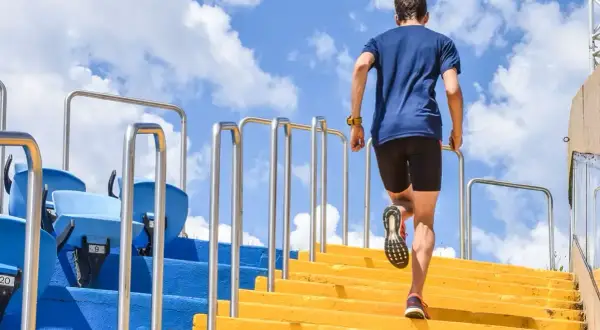 Un homme en tenue de sport monte des escaliers jaunes, un entraînement de renfo course à pied sous un ciel bleu.