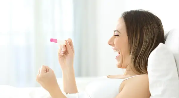 Kobieta z radością trzyma test ciążowy. To dowód, że jej marzenie o tym, jak zajść w ciążę, właśnie się spełnia!