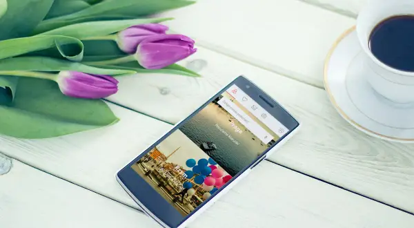 Telefon z aplikacjami przydatnymi w podróży, pokazujący Praga i Rzym. Obok bukiet tulipanów i filiżanka kawy.