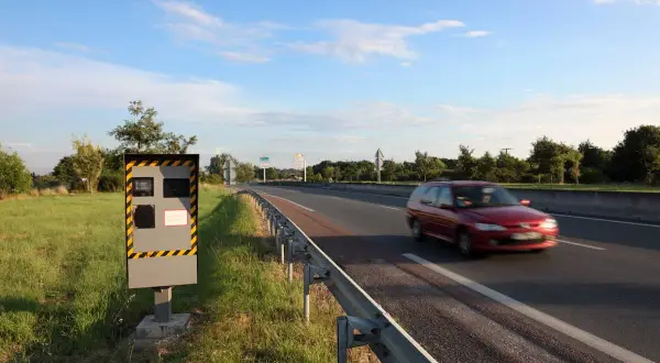 Un radar de chantier surveille la route. Une voiture rouge passe vite.