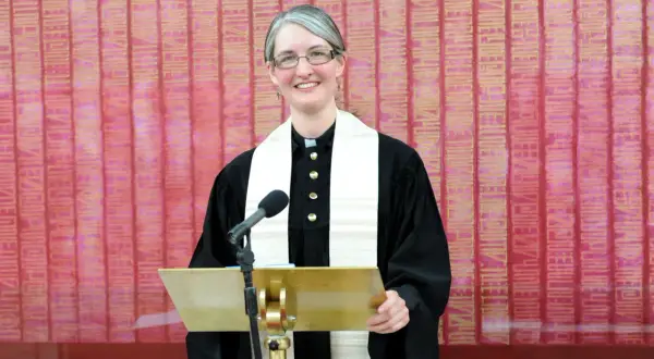 Eine Pfarrerin mit Brille und grauem Haar steht lächelnd hinter einem goldenen Pult. Sie trägt eine schwarze Robe und ein weißes Stola. In dir steckt ein guter Christ.