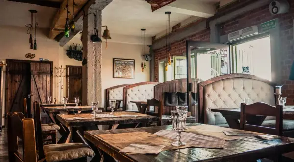 Wnętrze restauracji z drewnianymi stołami i wygodnymi kanapami. Na ścianie wisi model statku, nawiązujący do morskiego klimatu, jak w gdańskim bowke.
