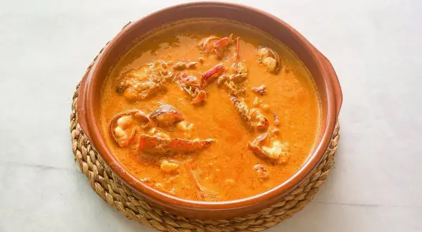 Caldereta de langosta, un plato de marisco reconfortante en una cazuela de barro, con trozos de langosta en una salsa naranja cremosa.