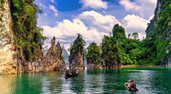 Khao Sok nationalpark med sina dramatiska kalkstensklippor och smaragdgröna vatten. Två små båtar glider fram på sjön.