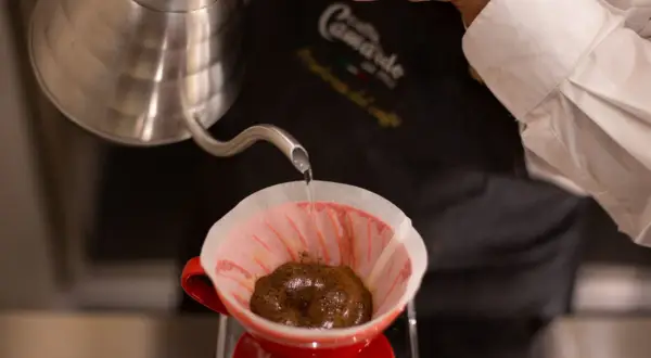 Versando acqua calda su caffè macinato in un filtro di carta rosso, per preparare un caffè filtro. Ecco come funziona la caffettiera americana.