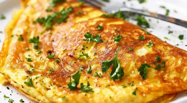En gyllene omelett, perfekt för ett snabbt omelett recept, toppad med färsk persilja och serverad på en vit tallrik med en gaffel.