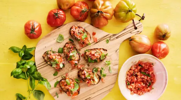 Bruschetta recept med färska tomater och basilika på en träskärbräda, omgivet av mogna tomater.