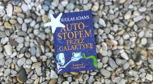Okładka książki "Autostopem przez galaktykę" Douglasa Adamsa, z ilustracją Chrisa Riddella, leży na kamieniach.