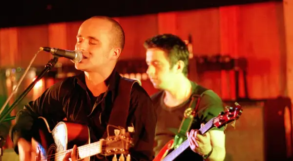 Wokalista z gitarą śpiewa do mikrofonu, i nawet kiedy będę sam, czuje wsparcie kolegi z zespołu.