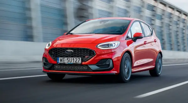 Czerwony Ford Fiesta ST pędzi po drodze, błyszcząc w słońcu.